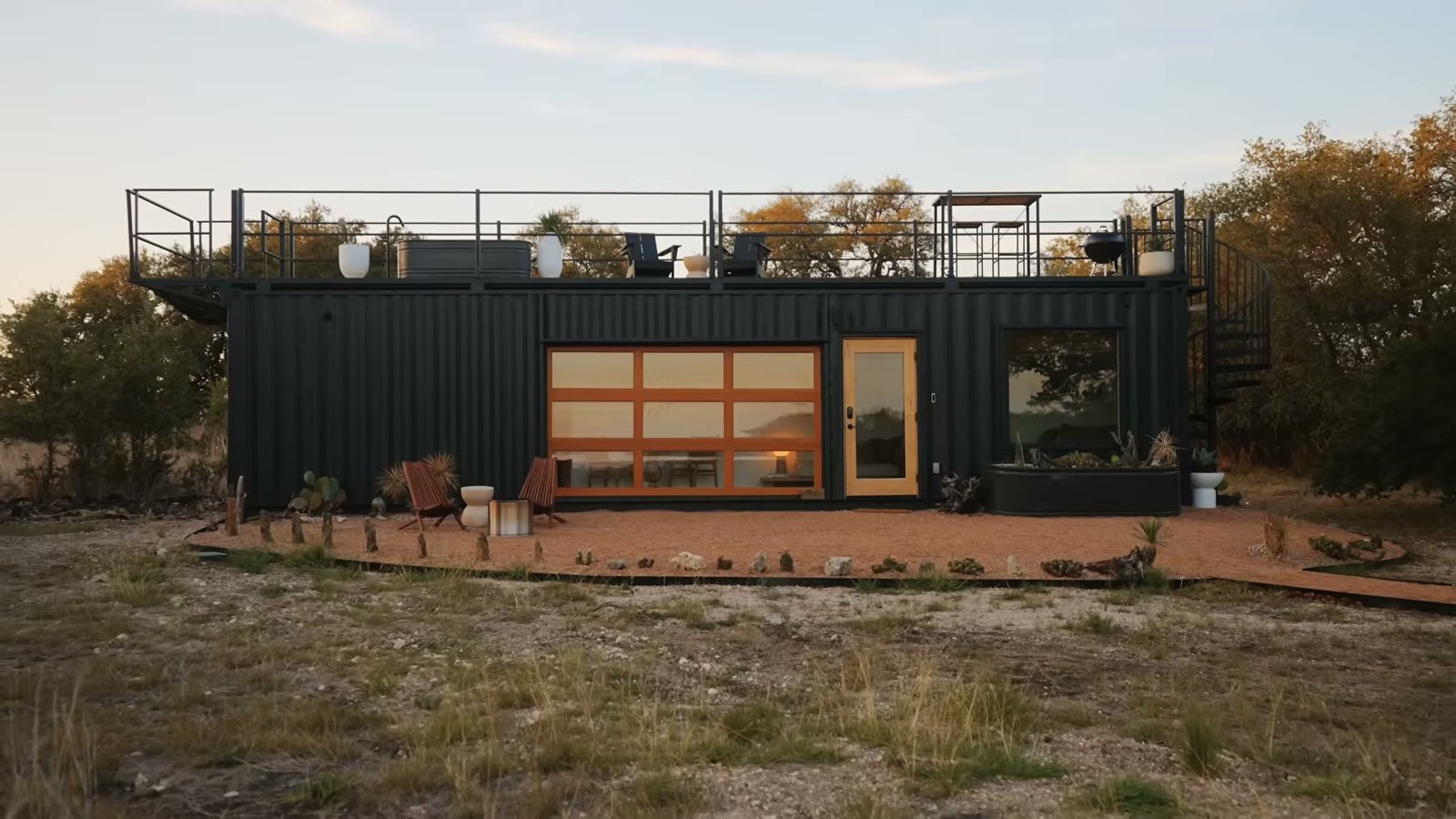 Black container home with timber-framed glazed doors in golden evening light